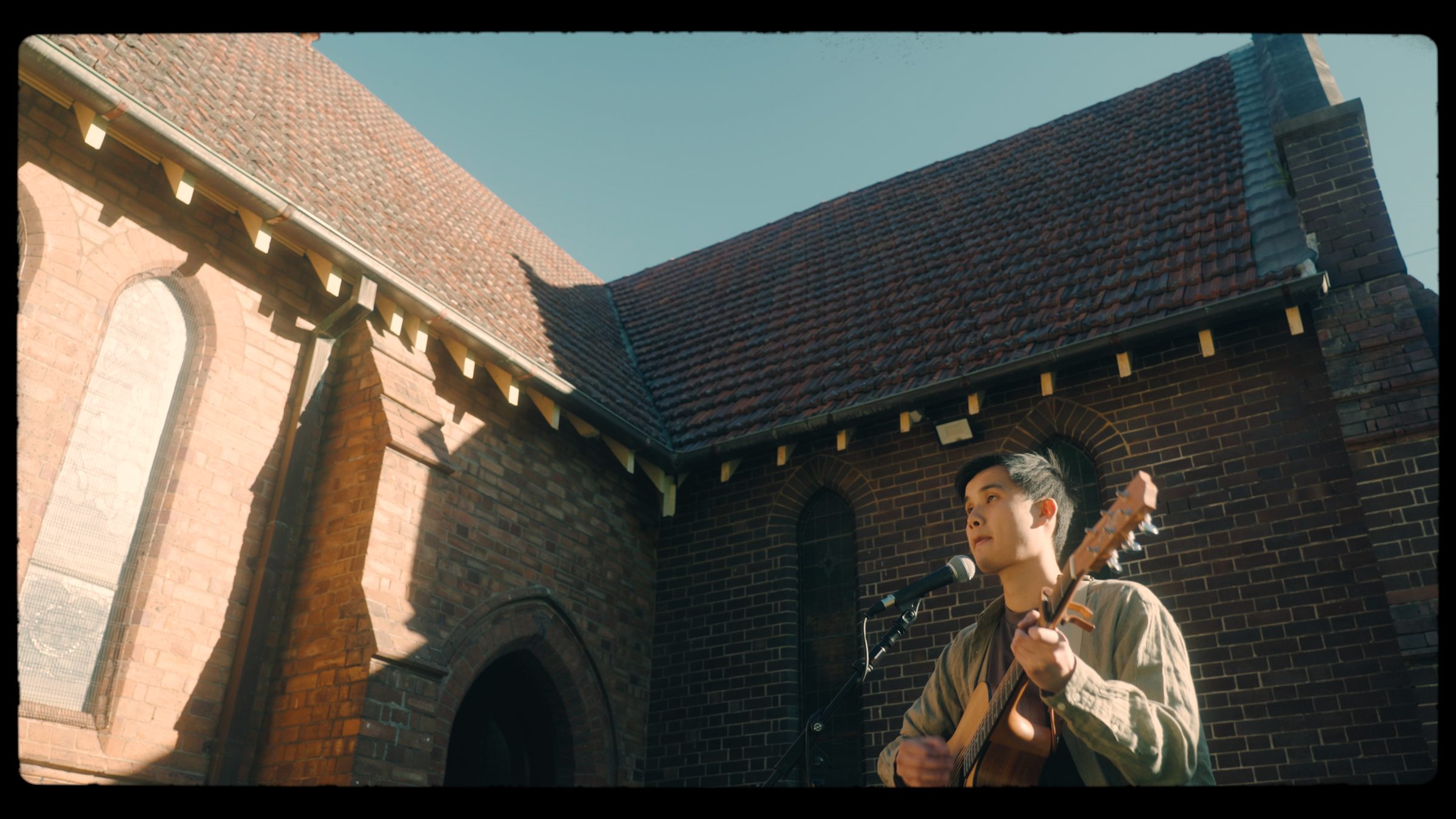 Daniel Chin playing guitar outside a brick church